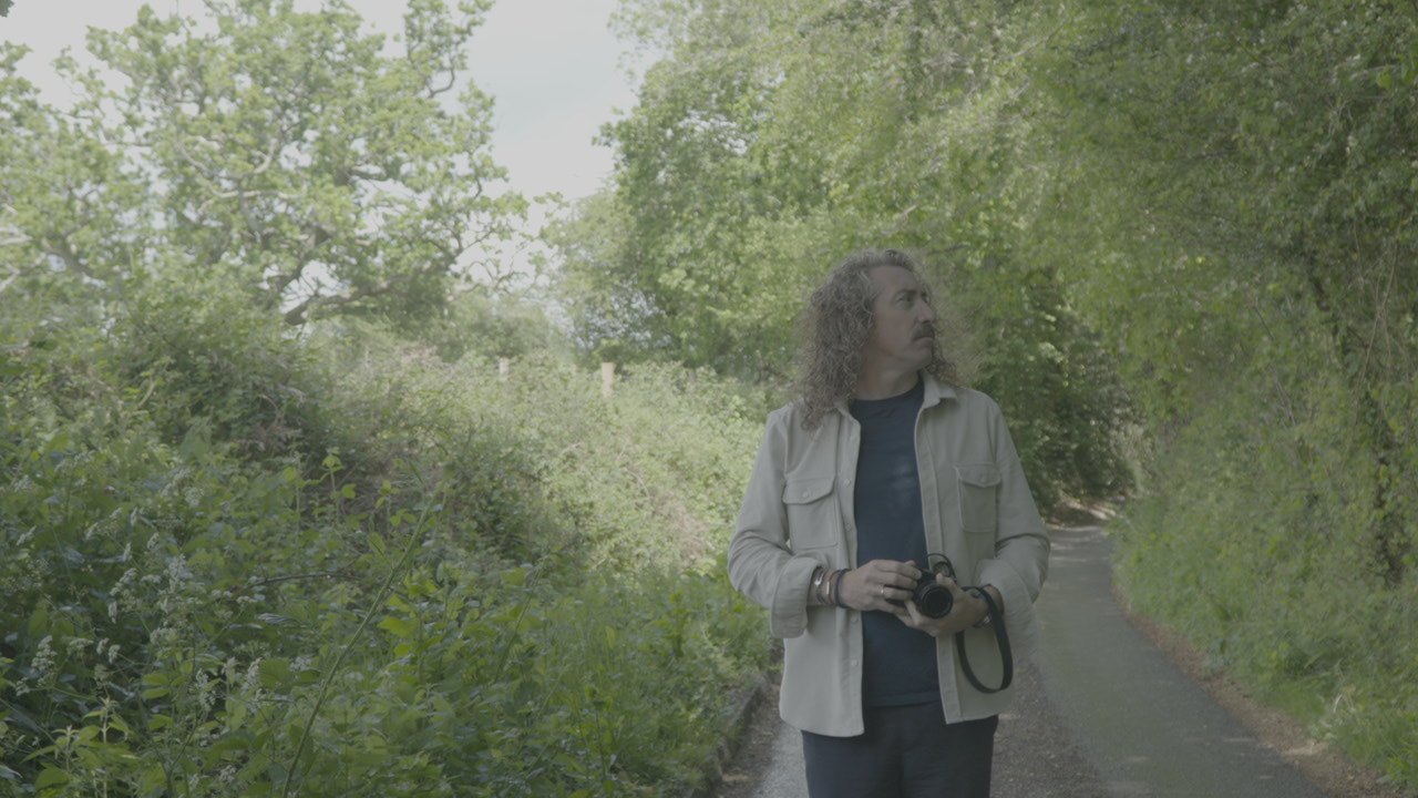 Andy Hooper walking a country lane with his camera